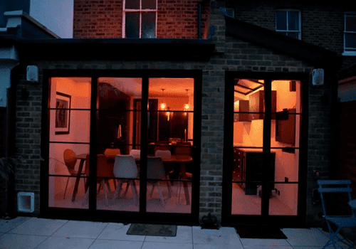 A housing extension that incorporates a dining room with warm orange lighting.