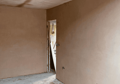Newly plastered walls in a bare room with a doorway in one corner.