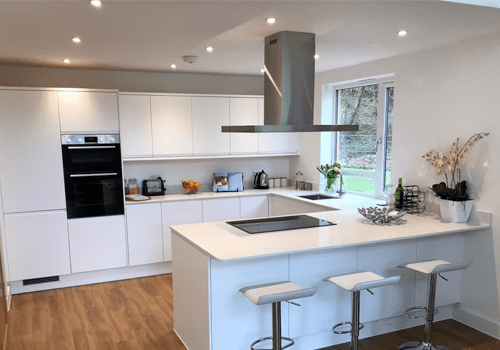 A large kitchen with three seats at an attached table. The kitchen is predominantly white.